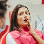 Close-up portrait of a sad young girl with a painful tooth, a doctor in office chairs, an isolated dentist office background clinic. Expressions of the human face, emotions, feelings, reactions